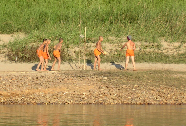 Junge Mönche beim Ballspiel am Flussufer