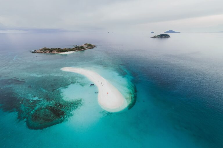 Luftaufnahme einer geschwungenen weißen Sandbank im türkisblauen Meer mit kleinen tropischen Inseln im Hintergrund