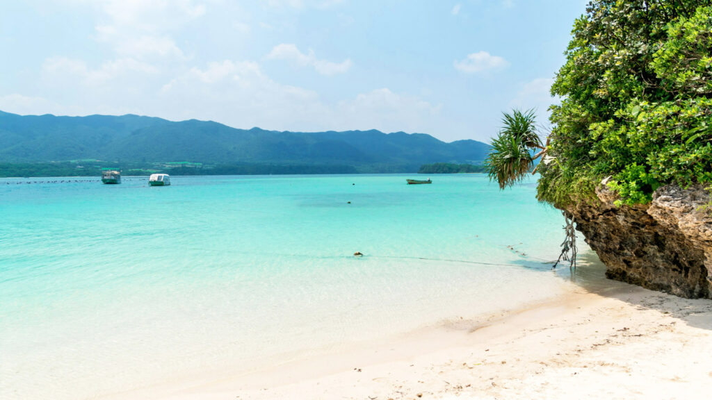 Weißer Sandstrand mit einem Felsen vor türkisem Meer