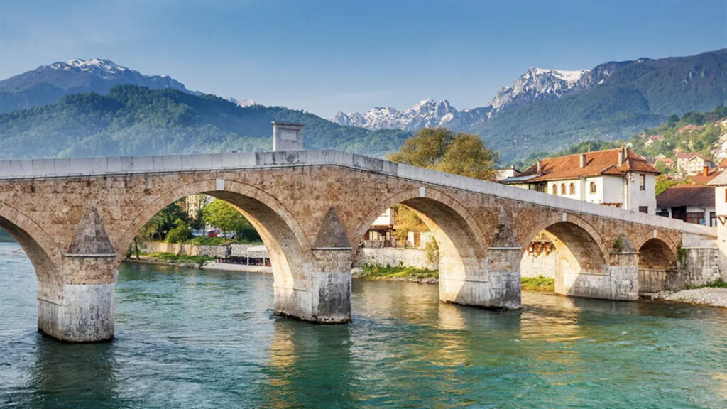 Brücke über türkisfarbenen Fluss mit Bergen im Hintergrund in Bosnien