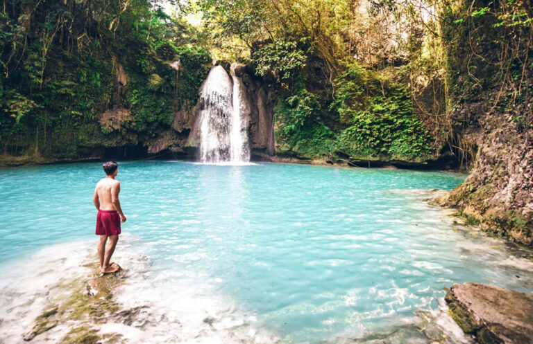 Mann in Badehose vor Lagune mit Wasserfall