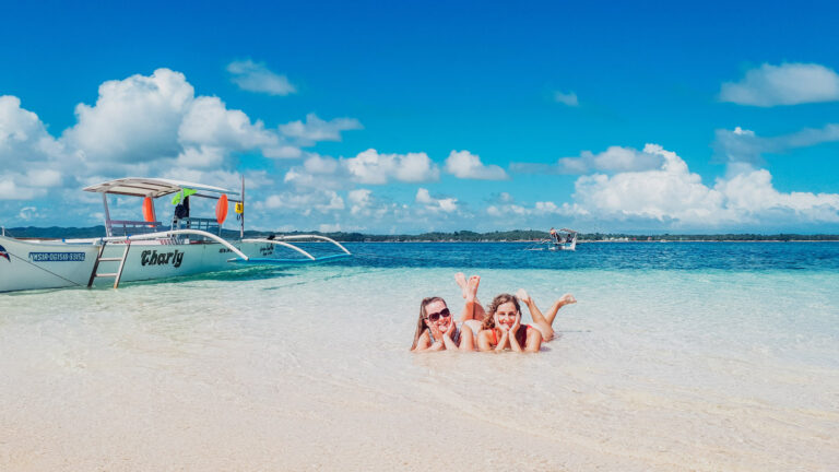 Zwei Mädels im seichten Wasser am Strand von Boracay neben traditionellem Boot