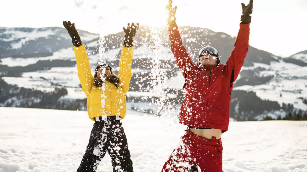 Ein Mann und eine Frau in Skiklamotten werfen Schnee in die Luft