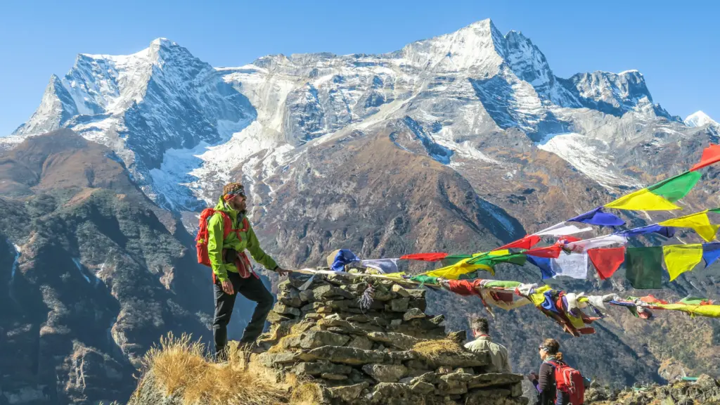 Nepal Trekking Gruppe auf Bergwanderung im Himalaya mit buddhistischen Gebetsfahnen und verschneiten Gipfeln im Hintergrund