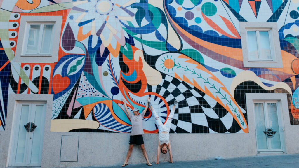 Zwei Reisende (einmal im Kopfstand, eimal mich hochgereckten Armen) vor Street Art in Porto