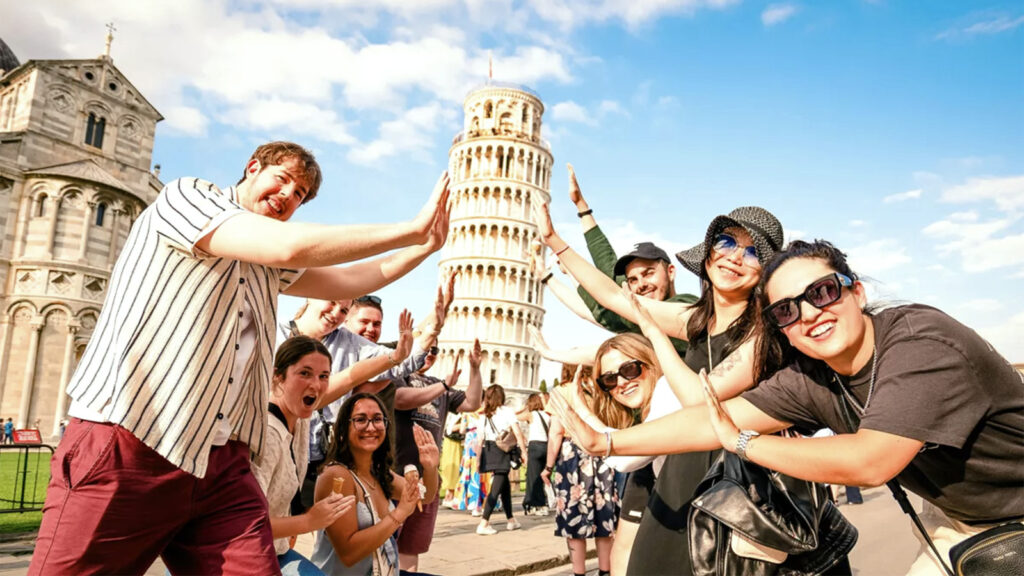 Gruppenfoto mit jungen Leuten, die so tun, als würden sie den schiefen Turm von Pisa stützen