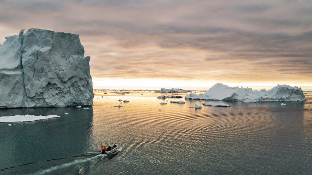 Kleines Boot vor Eisbergen in Grönland bei Sonnenuntergang