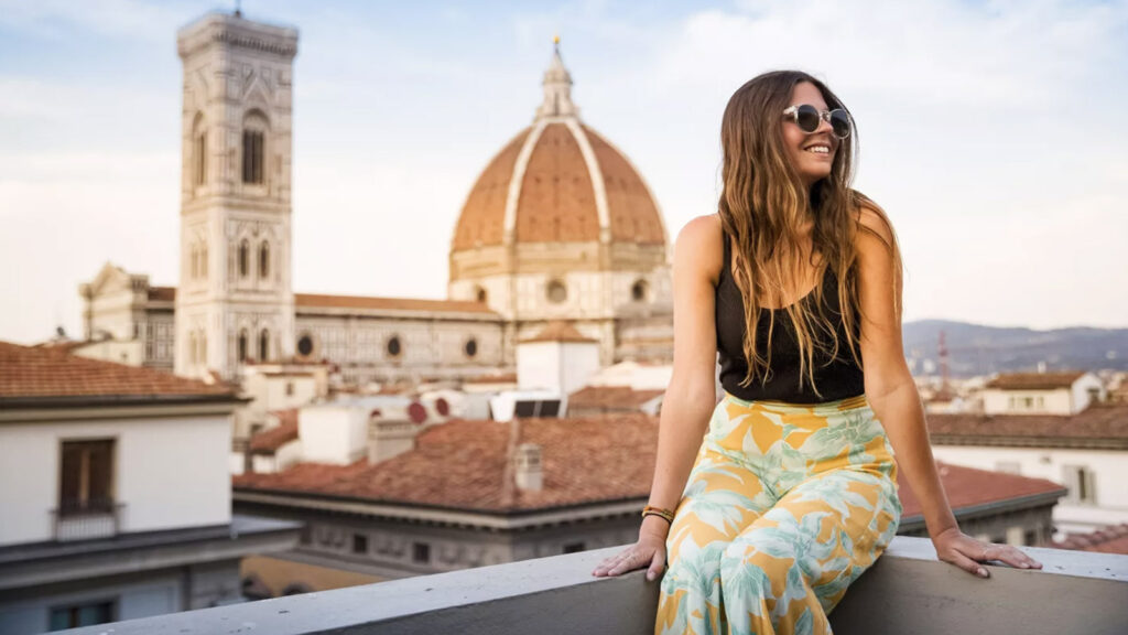 Junge Frau sitzt auf Steinmauer mit Blick auf den Dom von Florenz