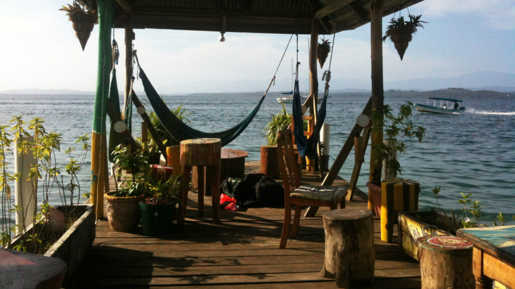 Hängematte auf Steg mit Tisch und Hockern aus Holz, Blick aufs Meer