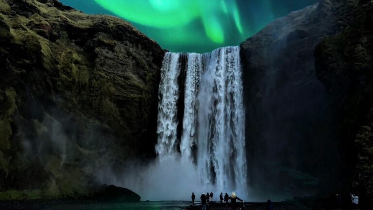 Abenteuerurlaub in Island: Abenteurer am Skógafoss und darüber grüne Polarlichter