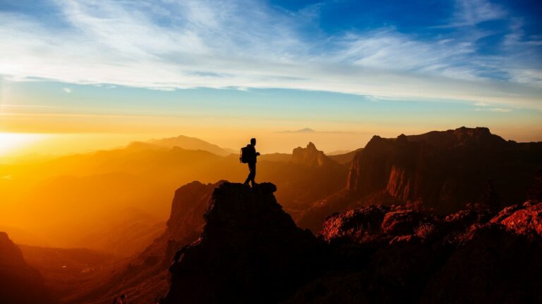 Person mit einem Backpacker Rucksack umgeben von Bergen bei Sonnenuntergang