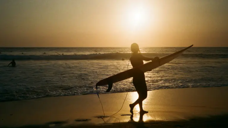Surfer mit Surfbrett bei Sonnenuntergang am Strand von Canggu auf Bali – Sumatra und Bali Erlebnisreise für junge Leute