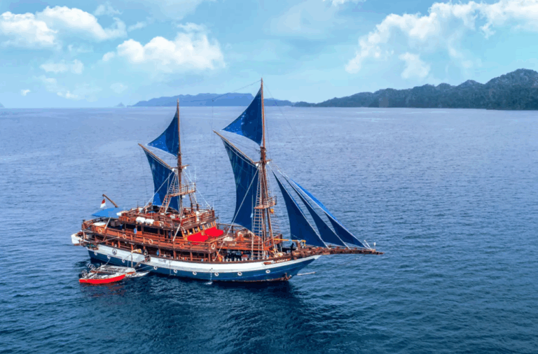 Traditionelles Segelschiff mit blauen Segeln auf dem Meer vor Raja Ampat, Indonesien – traumhafte Aussicht während eines Raja Ampat Urlaubs