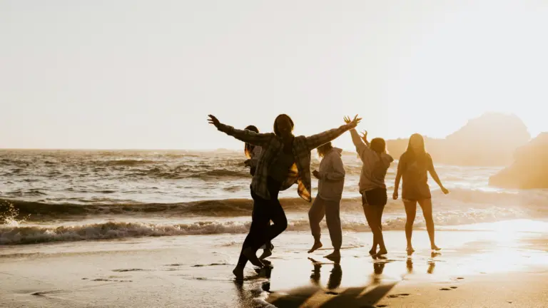 Gruppe junger Erwachsener am Strand, die bei Sonnenuntergang ausgelassen feiern und eine weltweite Jugendreise ab 18 genießen.