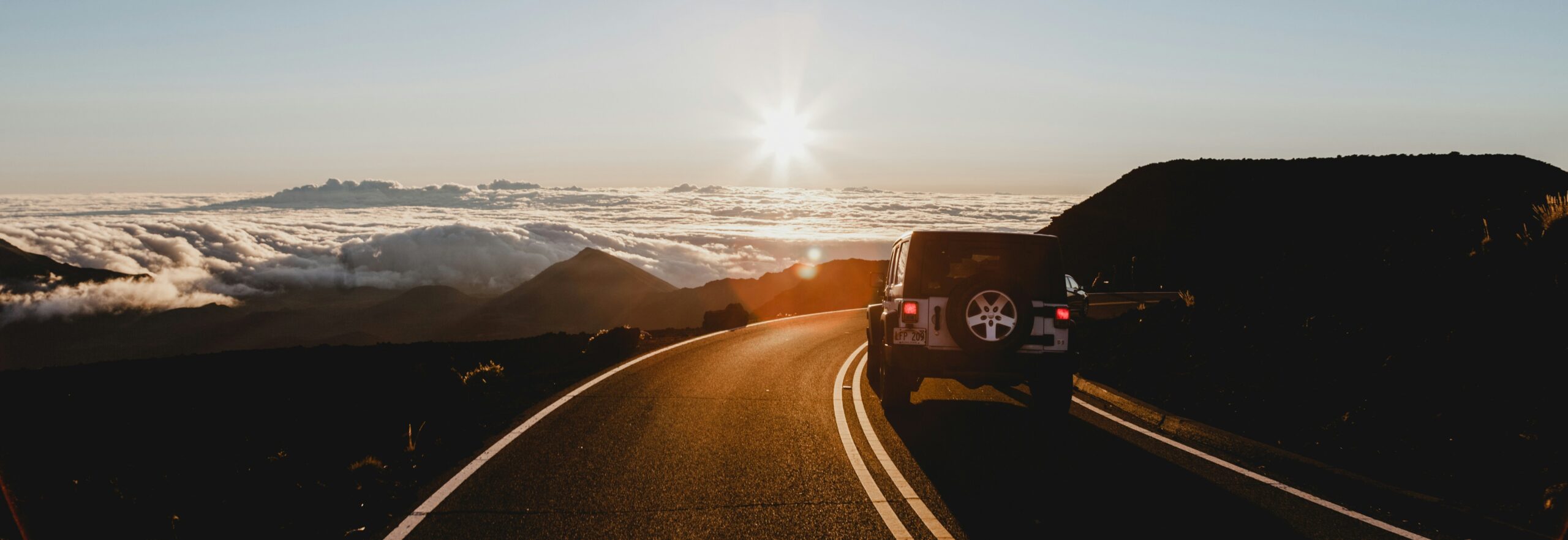 Mietwagenrundreise auf kurviger Panoramastraße über den Wolken bei Sonnenuntergang, Jeep auf traumhafter Route in den Bergen, Symbol für flexible und individuelle Roadtrips weltweit.