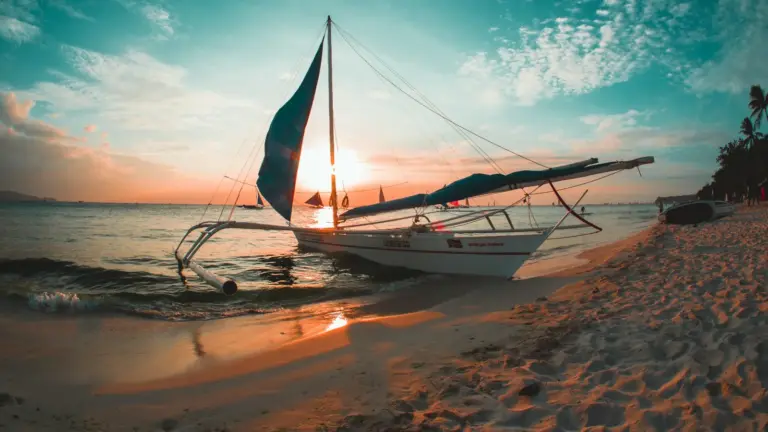 Traditionelles philippinisches Auslegersegelboot am White Beach auf Boracay bei Sonnenuntergang, mit Palmenstrand und türkisfarbenem Meer