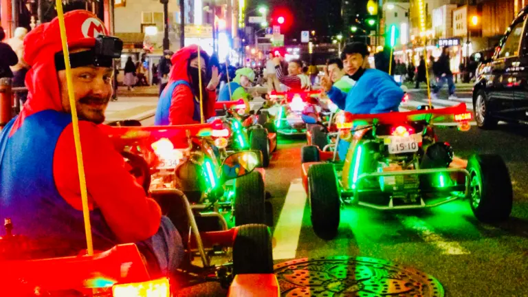 Junge Reisende in Super Mario Kostümen fahren abends mit beleuchteten Go Karts durch die Straßen von Tokio, Erlebnis einer Gruppenreise für junge Leute in Japan