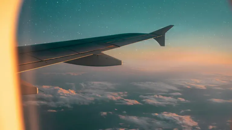 Blick aus dem Flugzeugfenster über die Tragfläche bei Sonnenuntergang, Symbolbild für Fernreisen in der Gruppe und sichere Reiseplanung