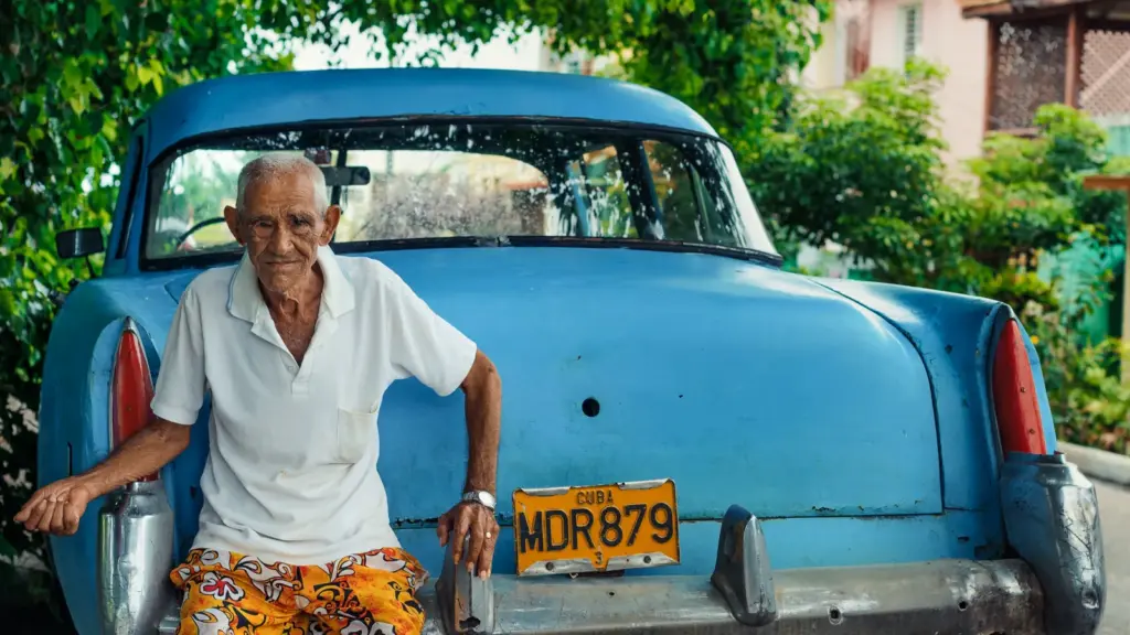 Älterer Mann vor einem blauen Oldtimer in Havanna auf Kuba