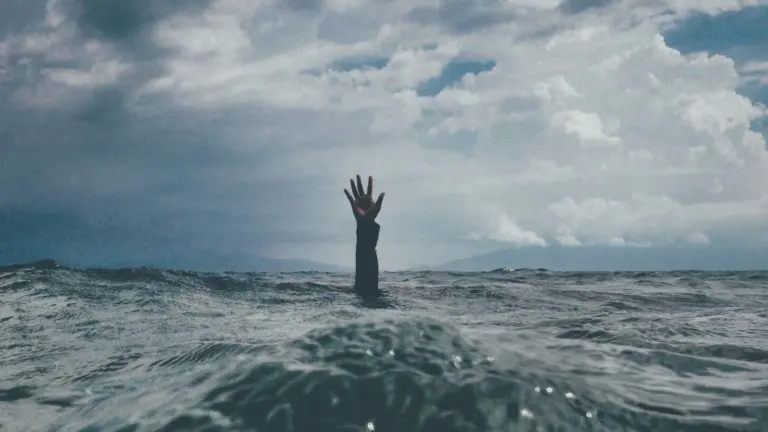Hand ragt aus stürmischem Meer als Symbol für Unsicherheit beim Reisen und warum organisierte Gruppenreisen mehr Sicherheit bieten