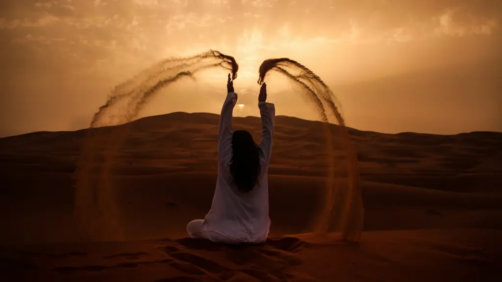 Frau sitzt in der Merzouga Wüste in Marokko auf einer hohen Düne und genießt ihre Gruppenreise junge Leute