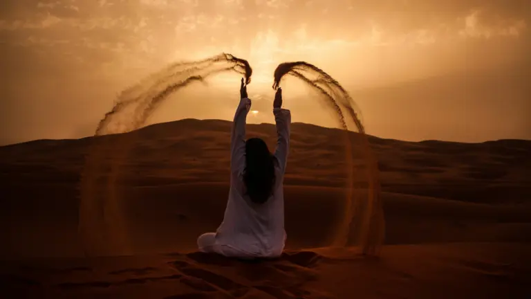 Frau sitzt in der Merzouga Wüste in Marokko auf einer hohen Düne und genießt ihre Gruppenreise junge Leute