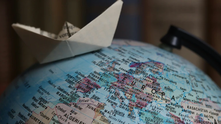 Papierboot auf Globus symbolisiert die Planung einer Weltreise und die Wahl der richtigen Route