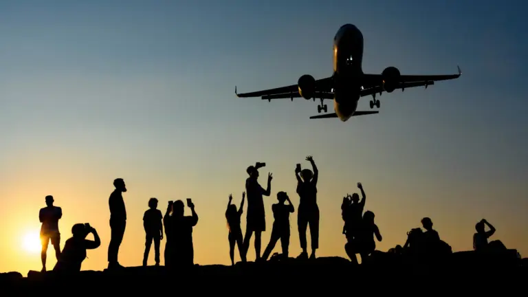 Silhouetten von Reisenden beobachten gemeinsam ein startendes Flugzeug bei Sonnenuntergang