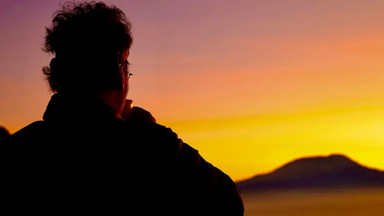 Silhouette einer Person beim Sonnenuntergang, die ruhig in die Ferne blickt und alleine reist