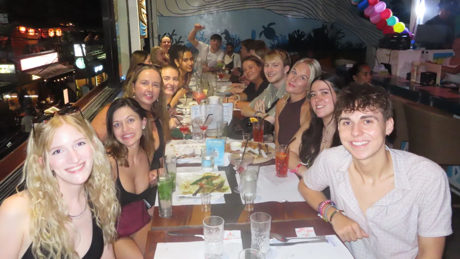 Junge internationale Reisegruppe sitzt gemeinsam beim Abendessen und lernt sich auf einer Gruppenreise kennen
