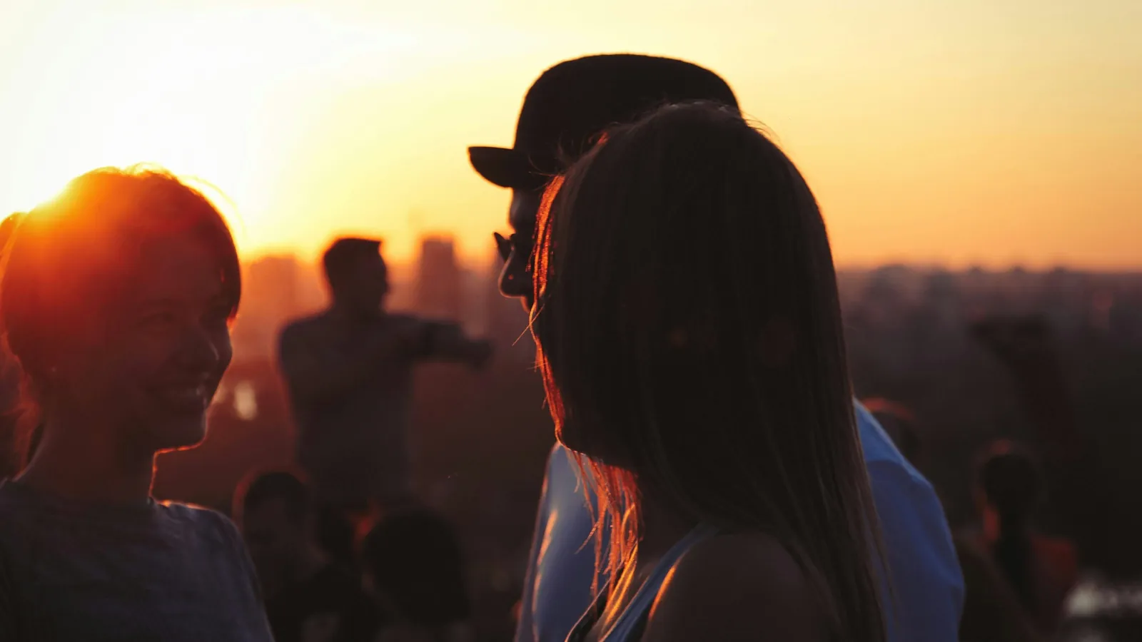 Junge Reisende genießen gemeinsam einen spontanen Abend auf einer Rooftop Bar bei Sonnenuntergang