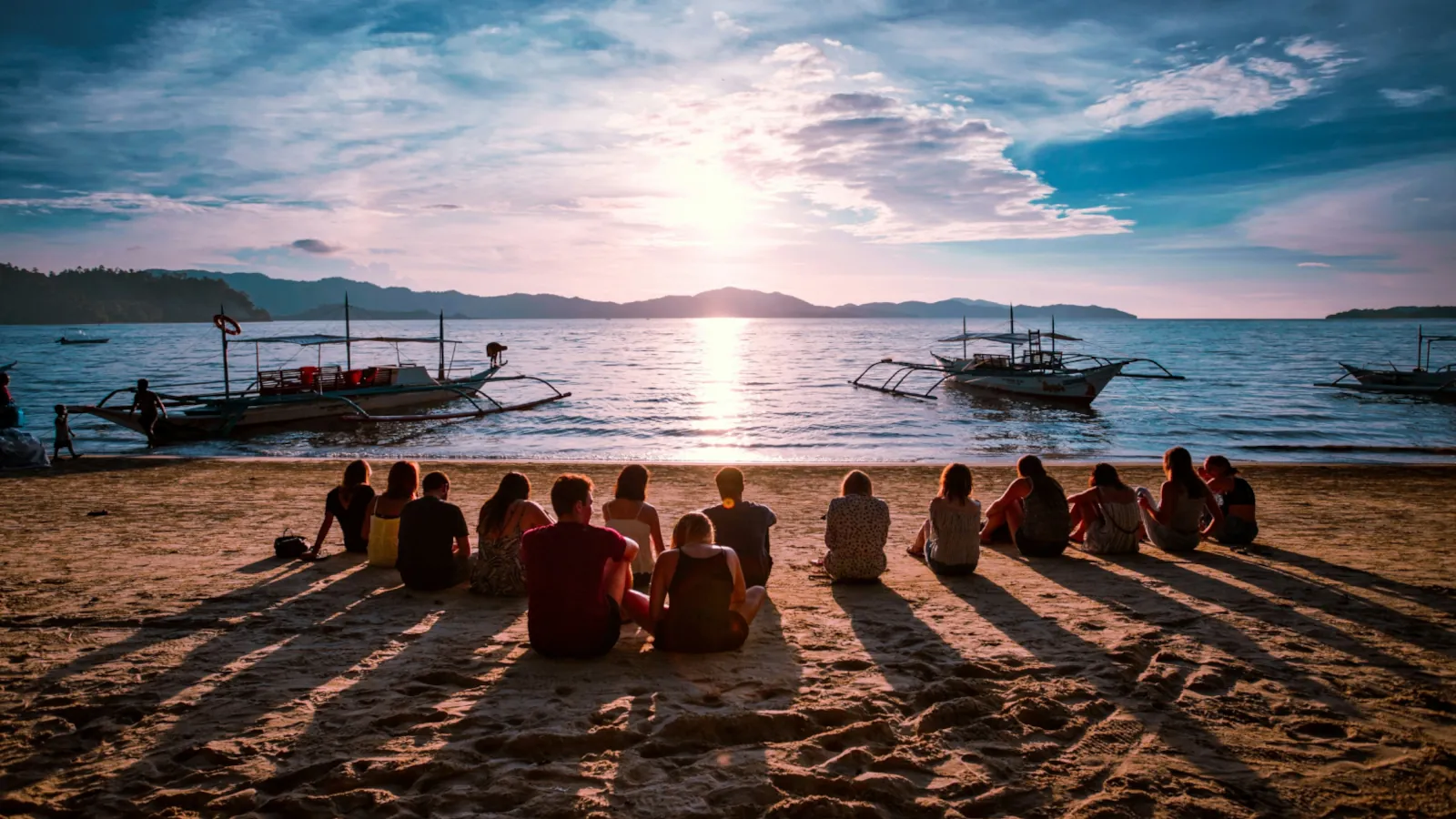 Junge Reisende sitzen gemeinsam bei Sonnenuntergang am Strand und genießen einen emotionalen Reisemoment