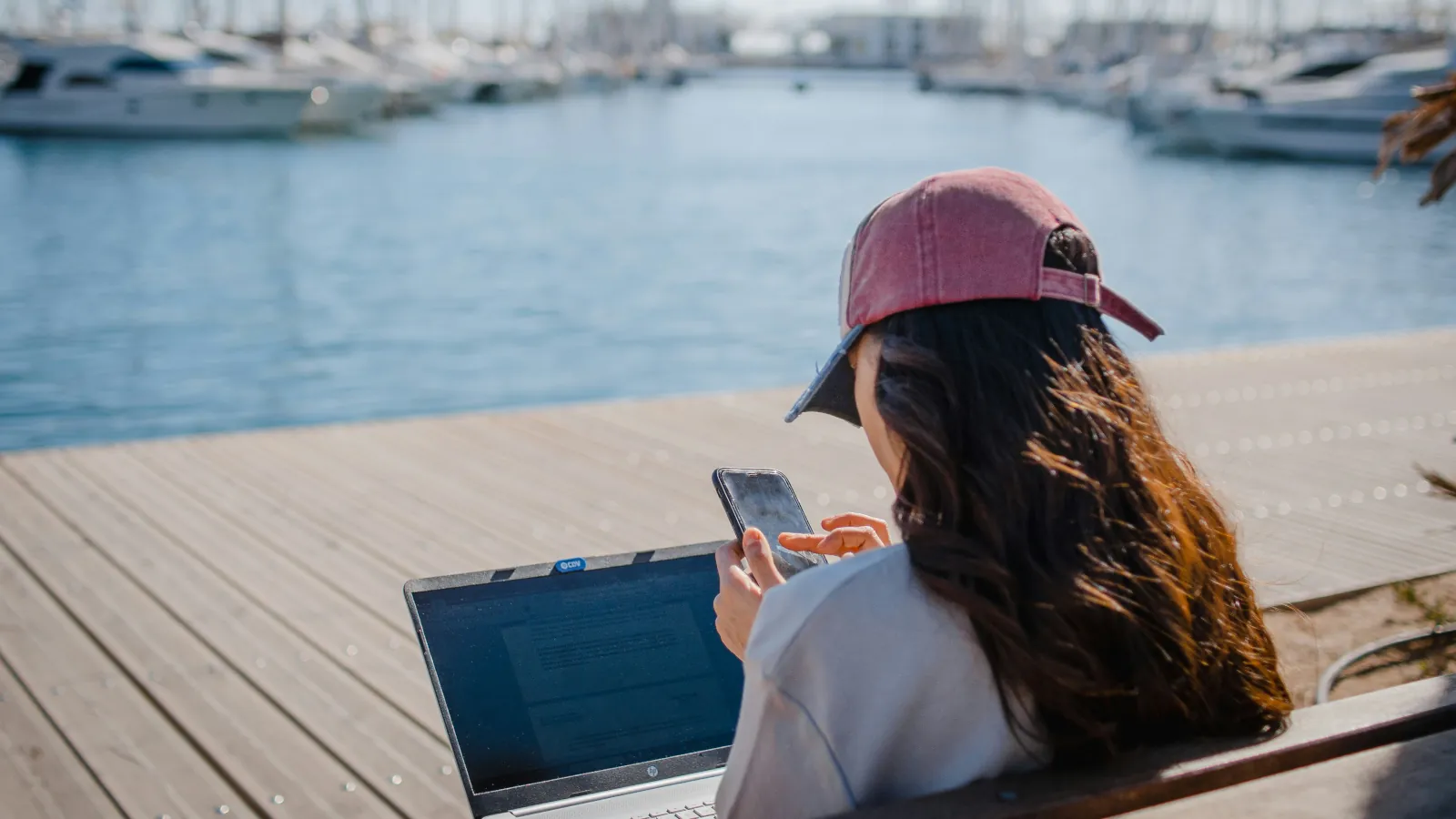 Junge Reisende plant mit Laptop und Smartphone ihre Weltreise am Hafen