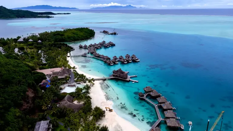 Drohnenaufnahme der türkisfarbenen Lagune von Bora Bora mit weißen Sandstränden und Overwater-Bungalows in Französisch-Polynesien.