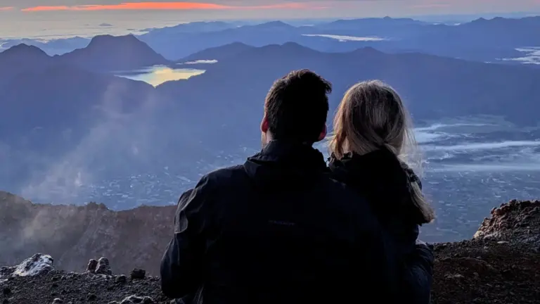 Reisendes Paar blickt beim Sonnenaufgang vom Gipfel des Mount Kerinci über die Vulkanlandschaft auf Sumatra