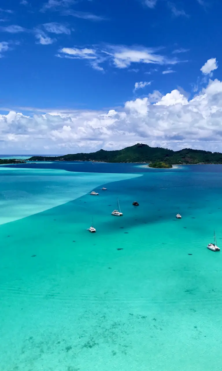 Mehrere Segelkatamarane ankern in der türkisfarbenen Lagune zwischen Tahaa und Raiatea in Französisch-Polynesien.