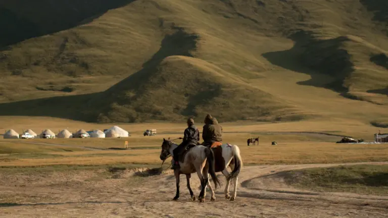 Zwei Reisende auf Pferden vor einem Jurtencamp in den Bergen Kirgisistans