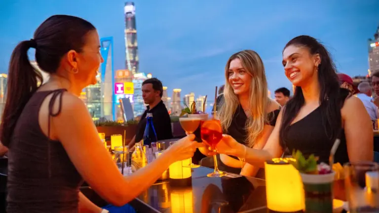 Junge Reisende beim gemeinsamen Drink in einer Rooftop Bar mit Blick auf die Skyline von Shanghai