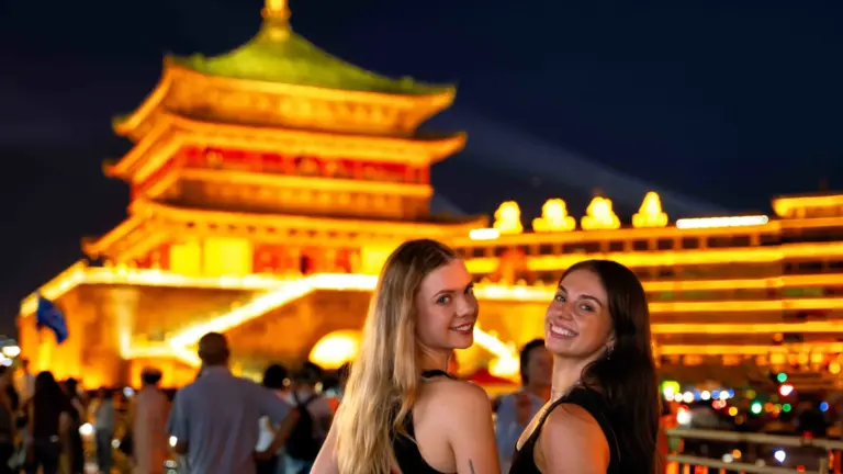 Zwei junge Reisende vor dem beleuchteten Glockenturm von Xi'an am Abend auf ihrer China Erlebnisreise