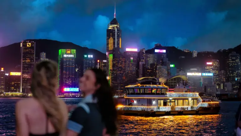 Nächtliche Skyline von Hongkong am Victoria Harbour mit beleuchtetem Ausflugsboot
