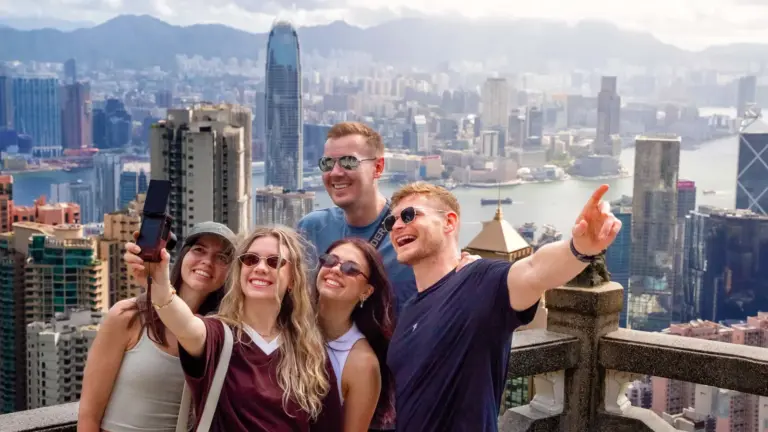 Junge Reisegruppe beim Selfie auf dem Victoria Peak mit Blick über Hongkong