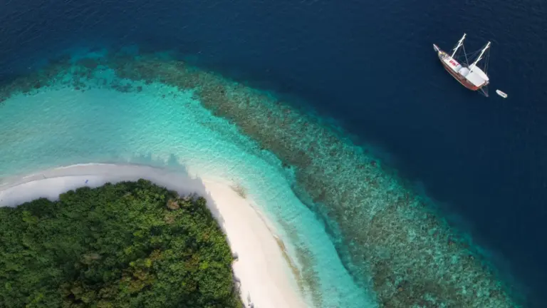 Luftaufnahme einer tropischen Insel mit weißem Sandstrand, Korallenriff und Expeditionsschiff im Süd Ari Atoll auf den Malediven